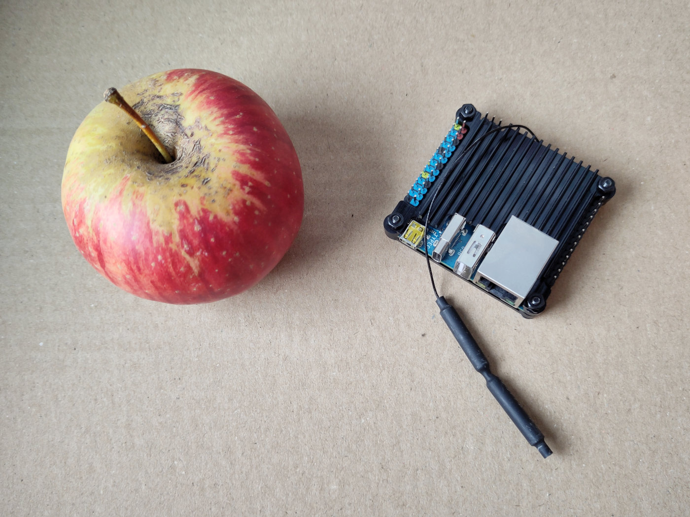A red and yellow apple and a small single board computer placed on
cardboard.